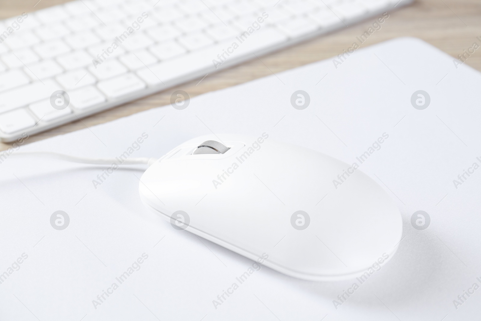 Photo of White computer mouse with mousepad and keyboard on wooden table, closeup