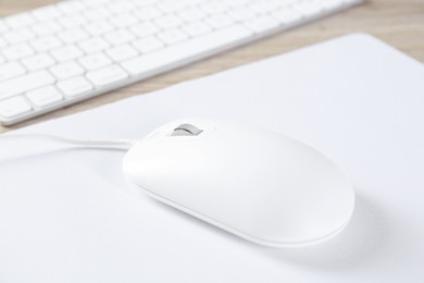 Photo of White computer mouse with mousepad and keyboard on wooden table, closeup