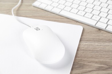 Photo of White computer mouse with mousepad and keyboard on wooden table, closeup