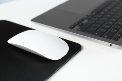 Photo of Computer mouse with mousepad and laptop on white table, closeup