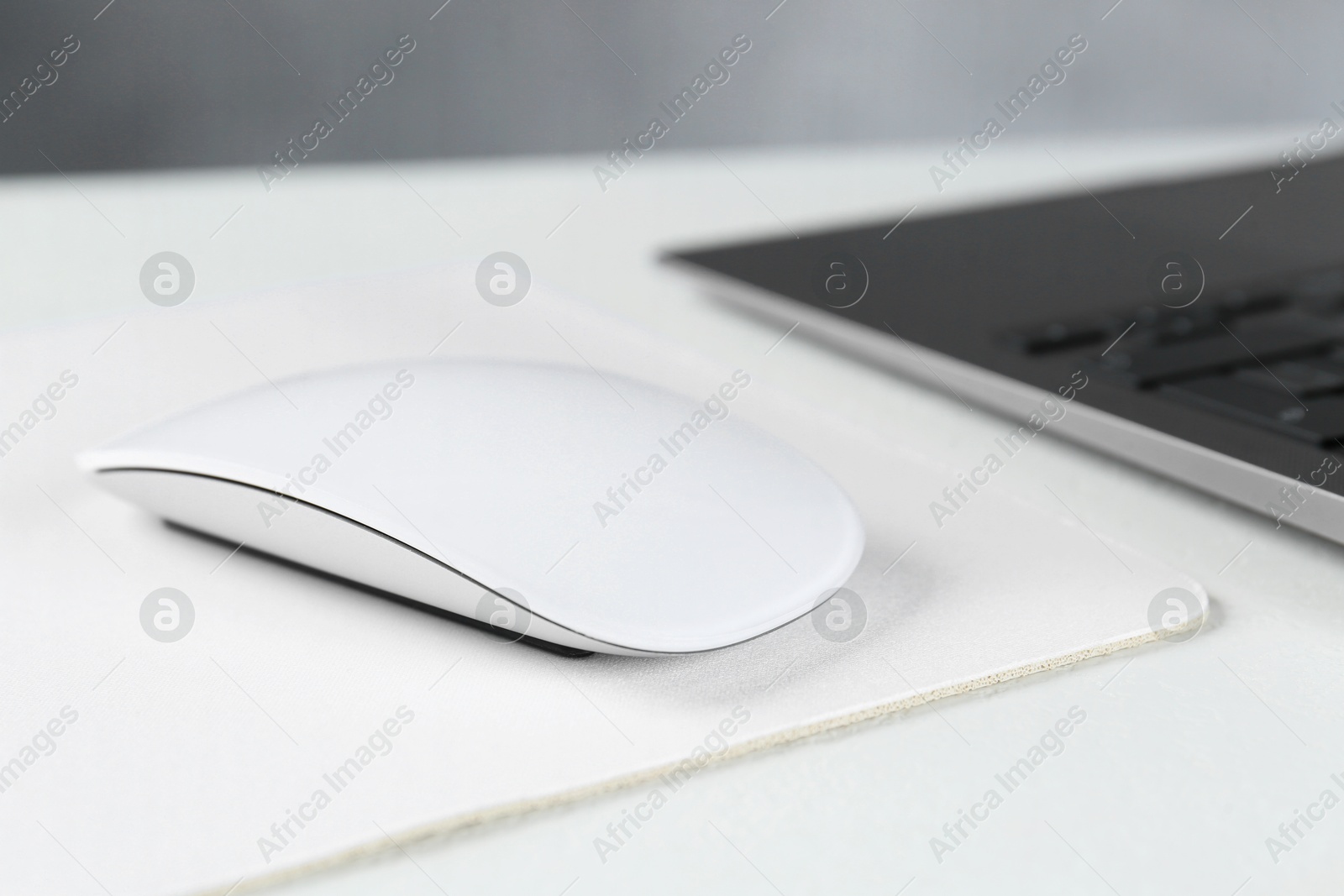 Photo of Computer mouse with mousepad and laptop on white table, closeup