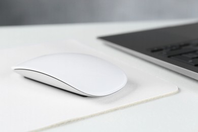 Photo of Computer mouse with mousepad and laptop on white table, closeup