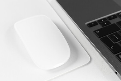 Photo of Computer mouse with mousepad and laptop on white table, closeup