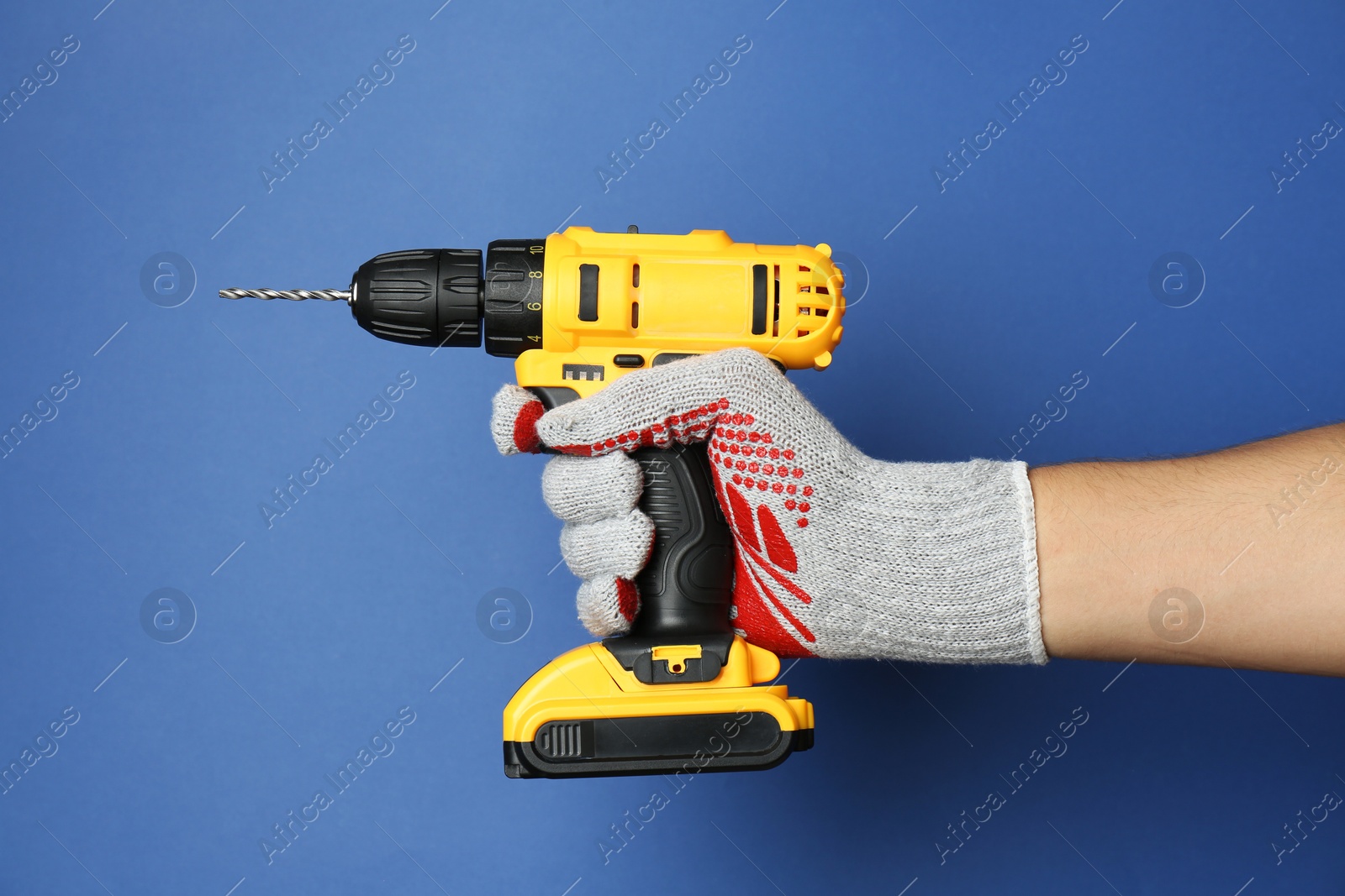 Photo of Man with cordless electric drill on blue background, closeup