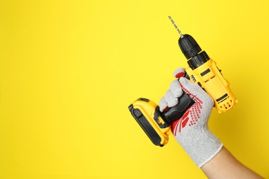 Photo of Man with cordless electric drill on yellow background, closeup. Space for text