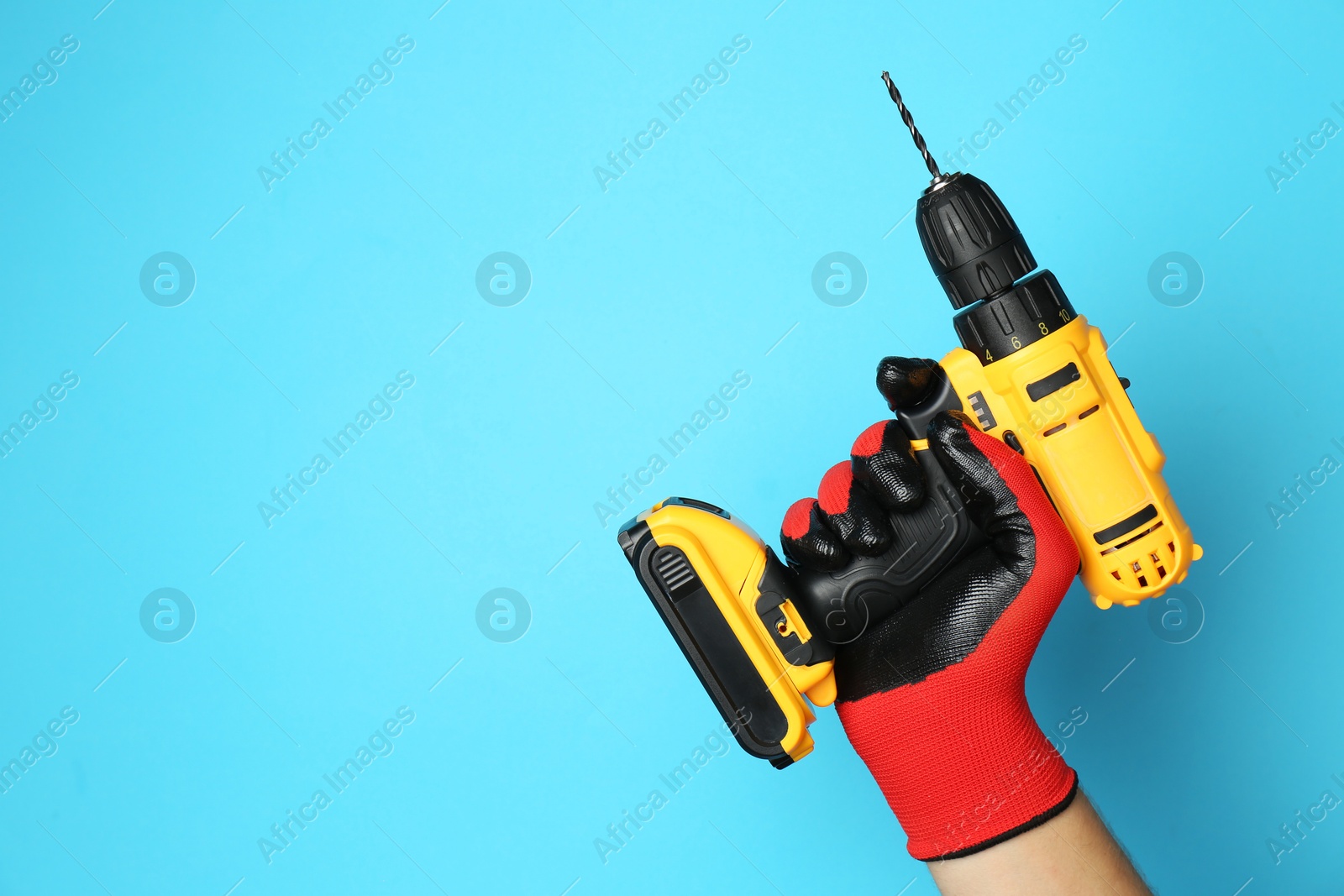 Photo of Man with cordless electric drill on light blue background, closeup. Space for text