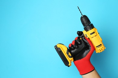 Man with cordless electric drill on light blue background, closeup. Space for text