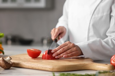 Photo of Professional chef cutting tomato at table in kitchen, closeup