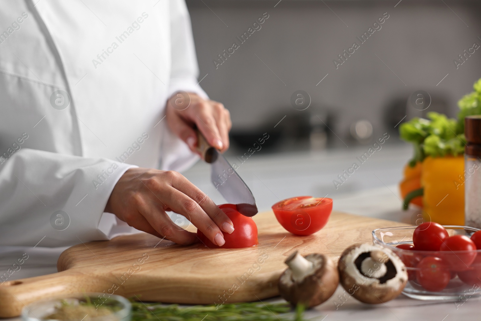 Photo of Professional chef cutting tomato at table in kitchen, closeup