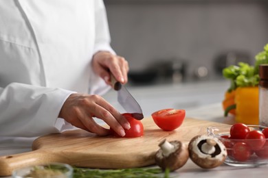 Professional chef cutting tomato at table in kitchen, closeup