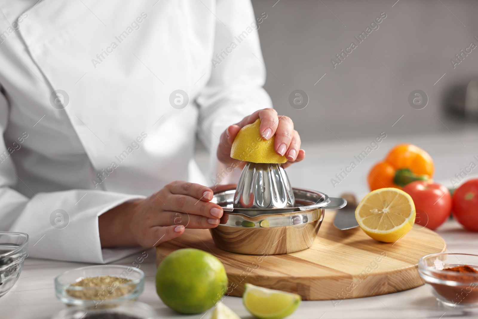 Photo of Woman squeezing juice out of lemon at table in kitchen, closeup