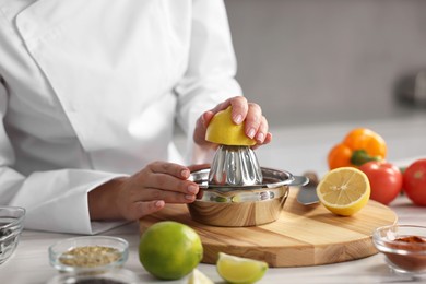 Woman squeezing juice out of lemon at table in kitchen, closeup