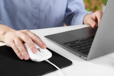 Photo of Woman using computer mouse while working with laptop at white table, closeup