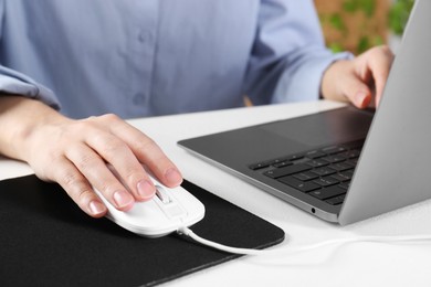 Photo of Woman using computer mouse while working with laptop at white table, closeup