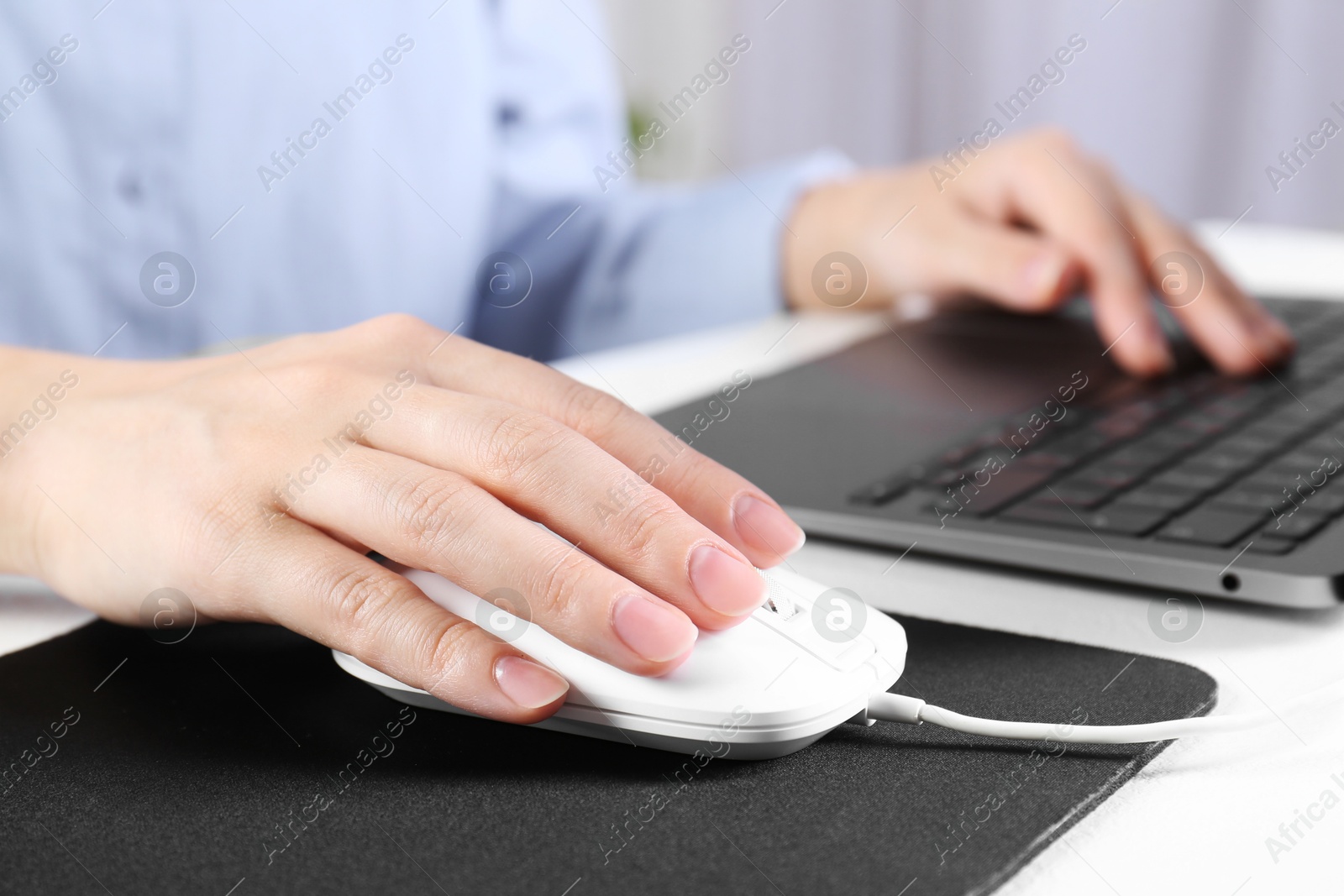 Photo of Woman using computer mouse while working with laptop at white table, closeup