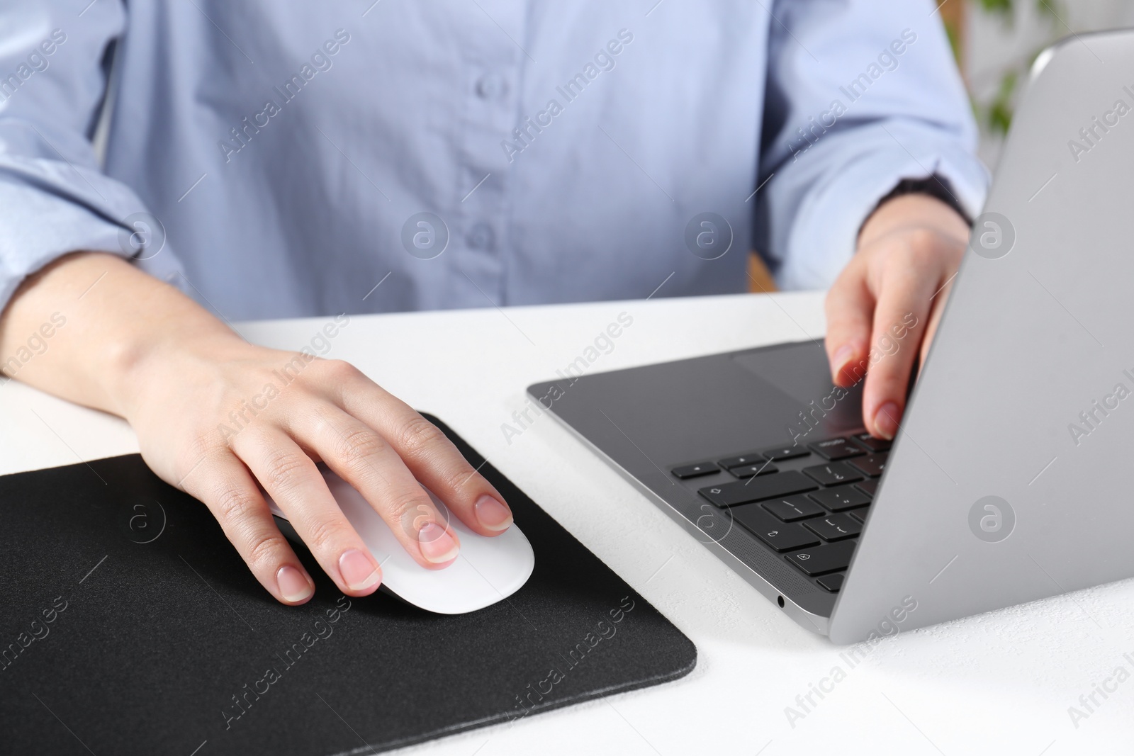 Photo of Woman using computer mouse while working with laptop at white table, closeup