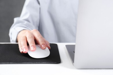 Photo of Woman using computer mouse while working with laptop at white table, closeup