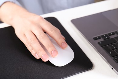 Photo of Woman using computer mouse while working with laptop at white table, closeup