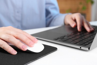 Photo of Woman using computer mouse while working with laptop at white table, closeup