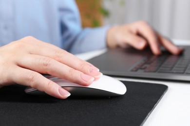 Photo of Woman using computer mouse while working with laptop at white table, closeup