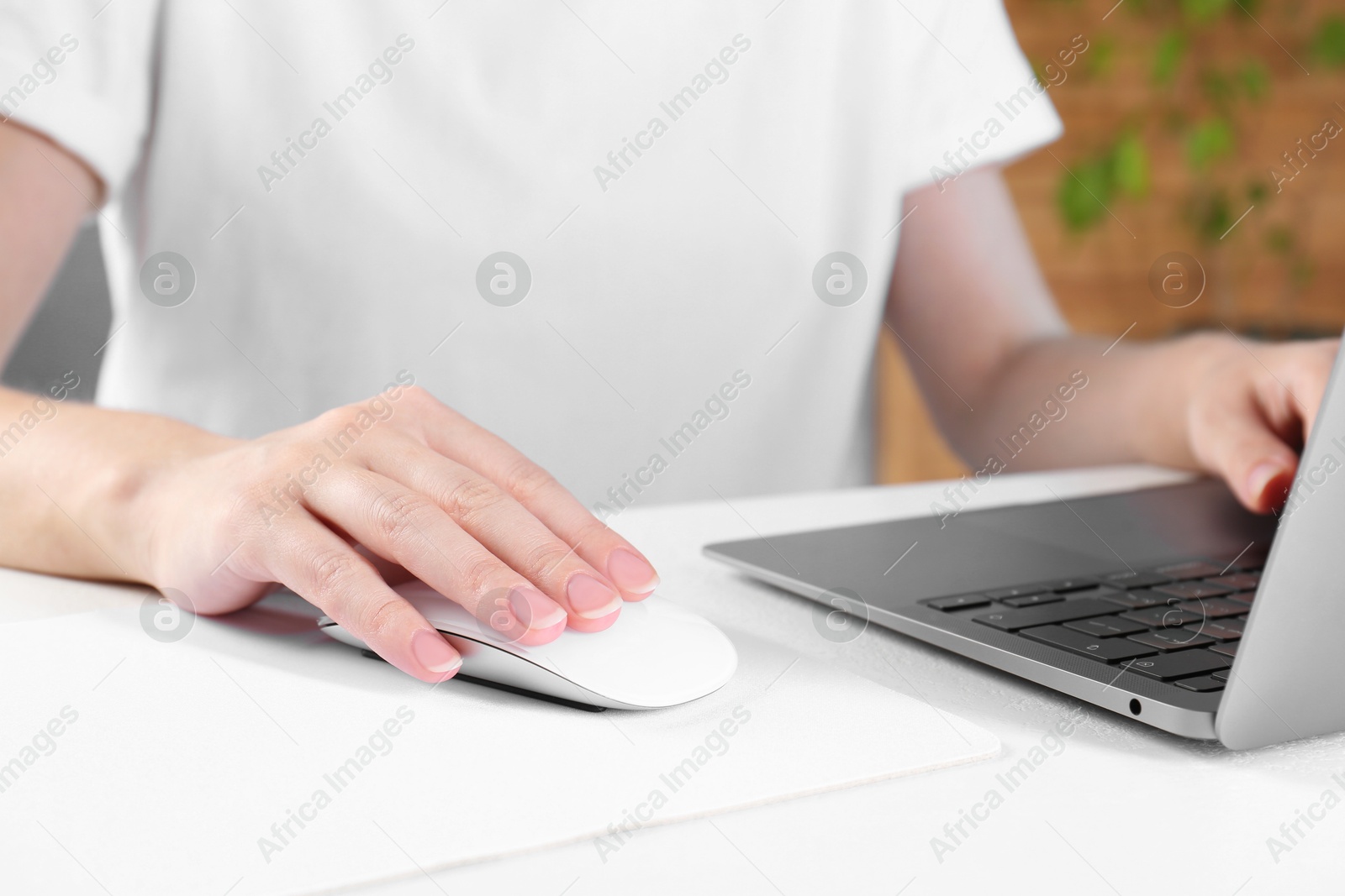 Photo of Woman using computer mouse while working with laptop at white table, closeup