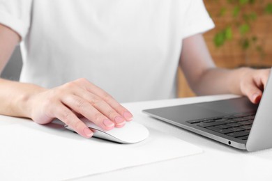 Photo of Woman using computer mouse while working with laptop at white table, closeup