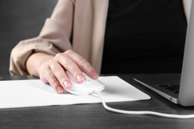 Photo of Woman using computer mouse while working with laptop at black wooden table, closeup