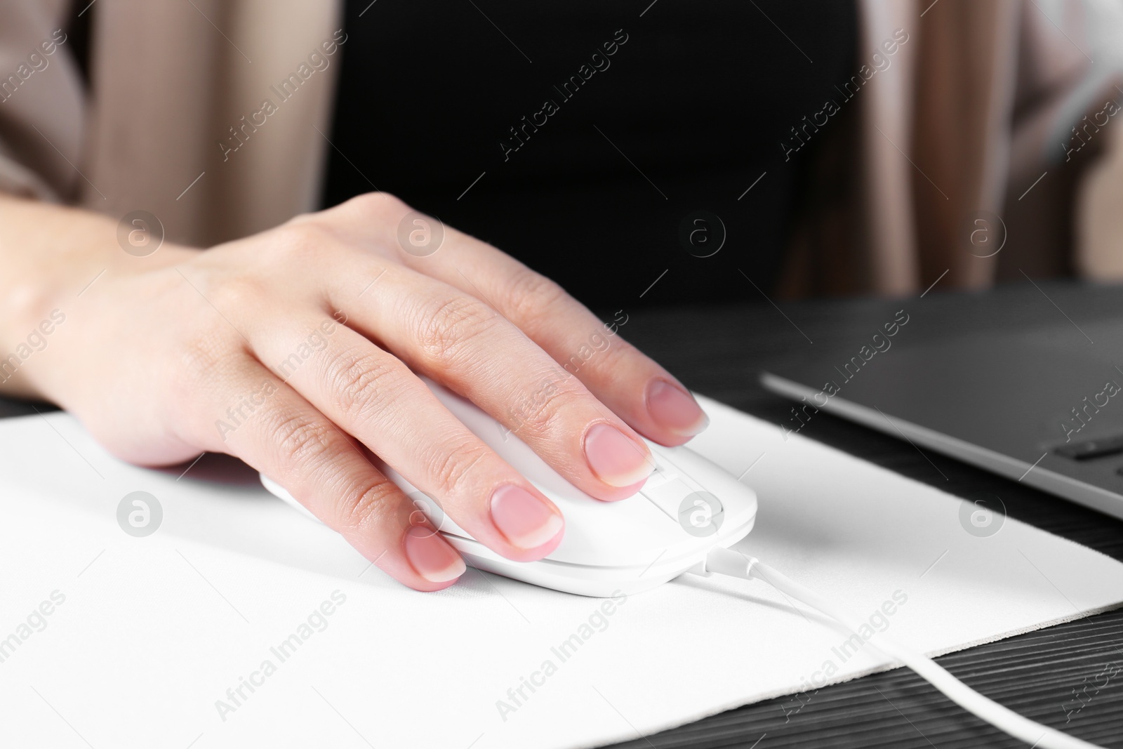 Photo of Woman using computer mouse while working with laptop at black wooden table, closeup