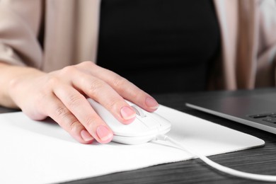 Photo of Woman using computer mouse while working with laptop at black wooden table, closeup