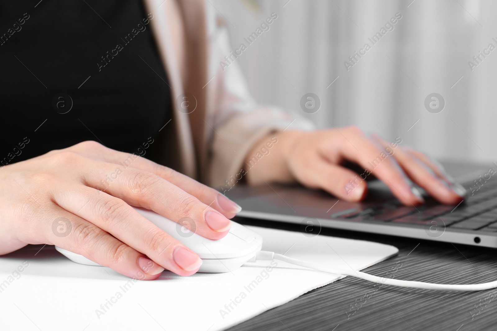 Photo of Woman using computer mouse while working with laptop at black wooden table, closeup