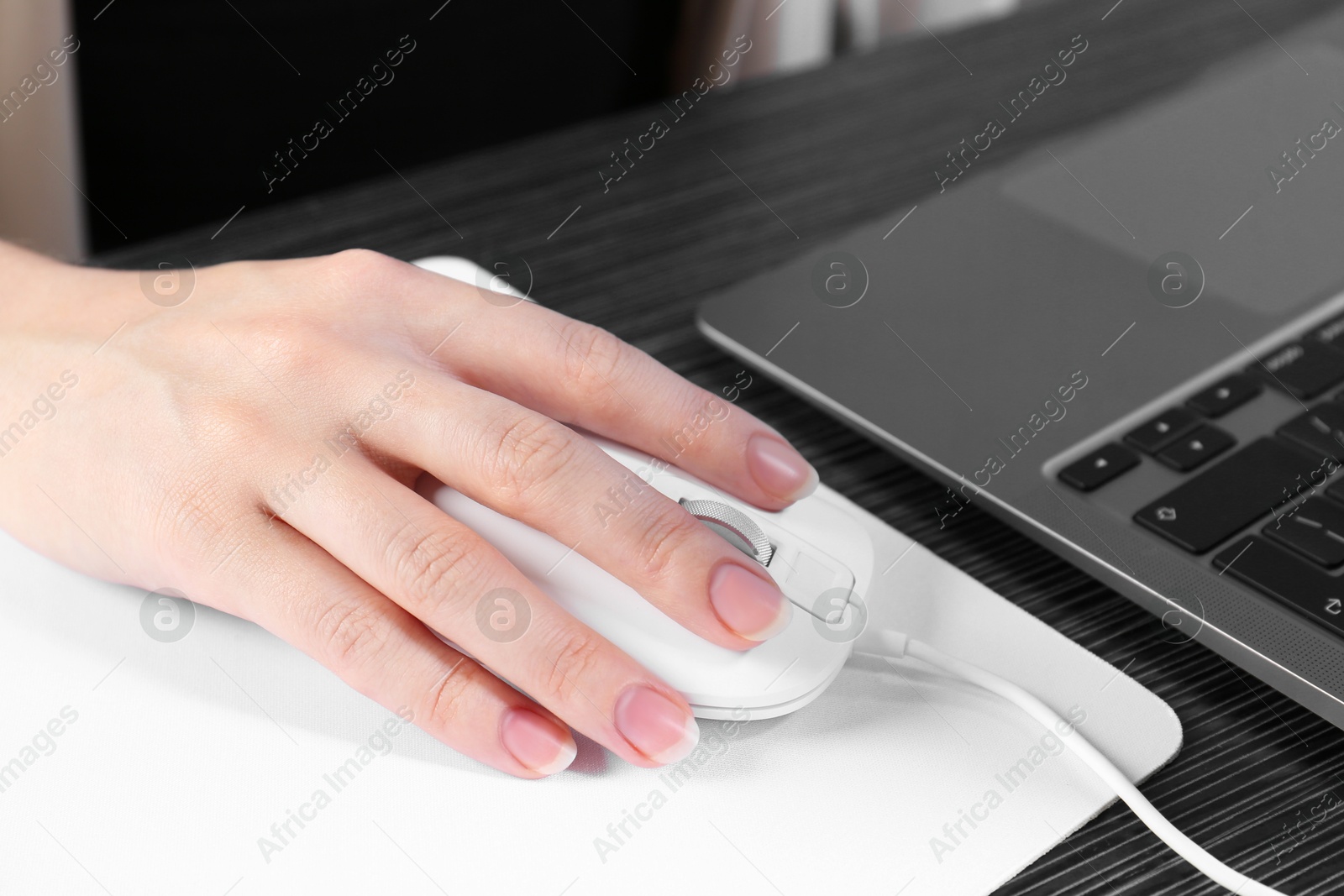 Photo of Woman using computer mouse while working with laptop at black wooden table, closeup