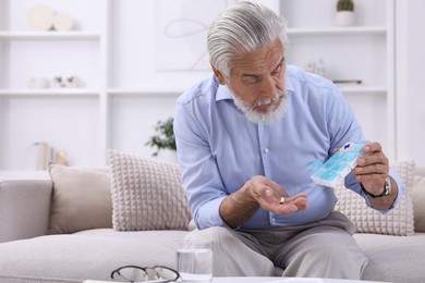 Photo of Senior man with pills and organizer on sofa at home