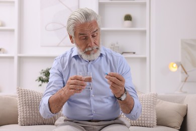 Photo of Senior man with glass of water and pill on sofa at home