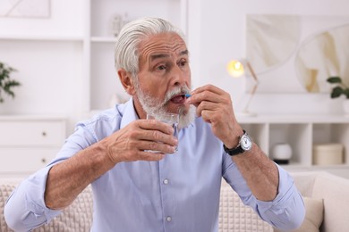 Senior man with glass of water taking pill at home