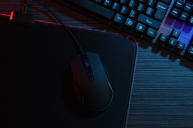 Photo of Computer mouse, mousepad and keyboard on dark wooden table in neon lights, flat lay