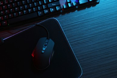 Photo of Computer mouse, mousepad and keyboard on dark wooden table in neon lights, flat lay. Space for text