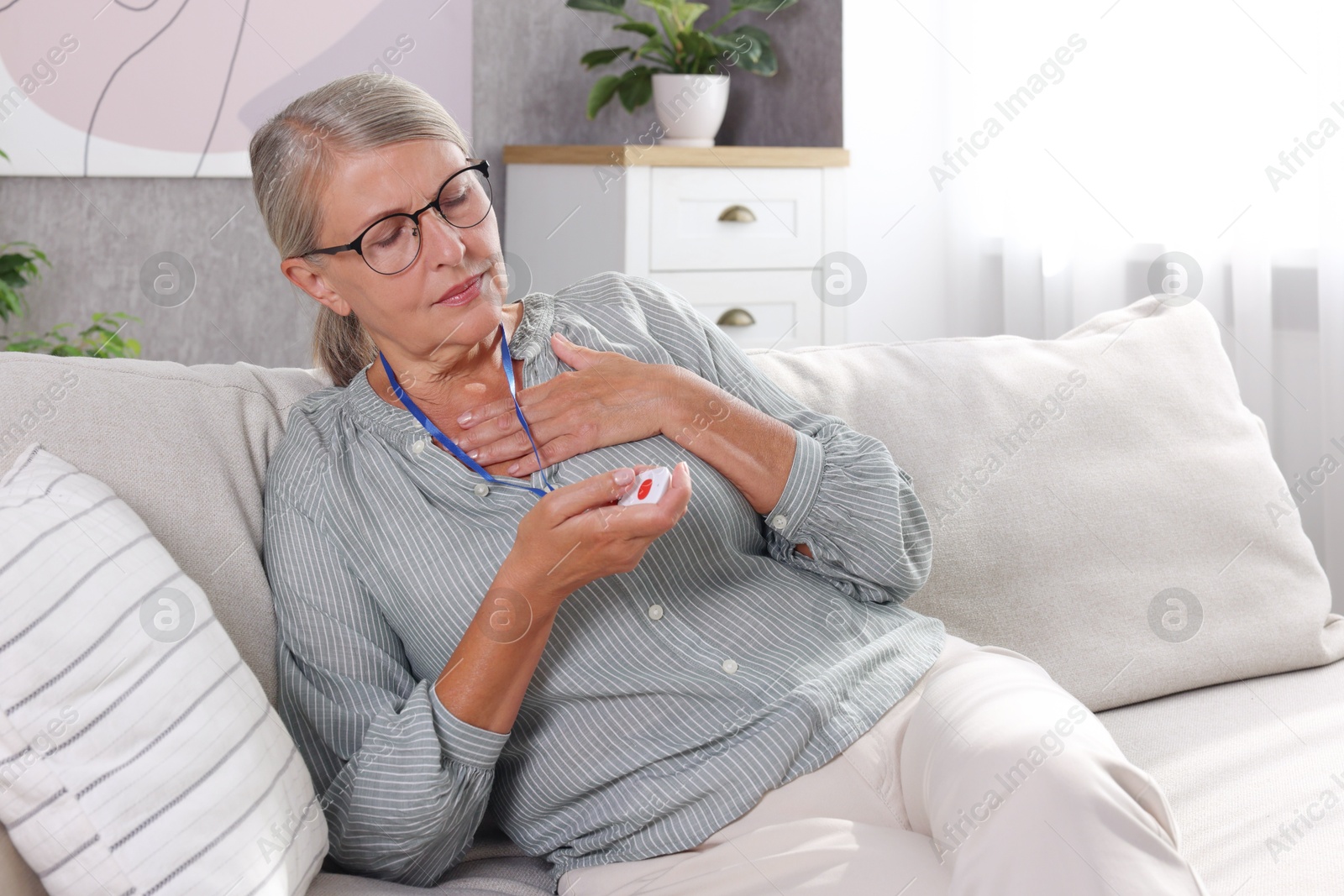 Photo of Senior woman suffering from heart pain pressing emergency call button at home