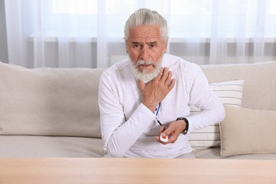 Photo of Senior man suffering from neck pain pressing emergency call button at home