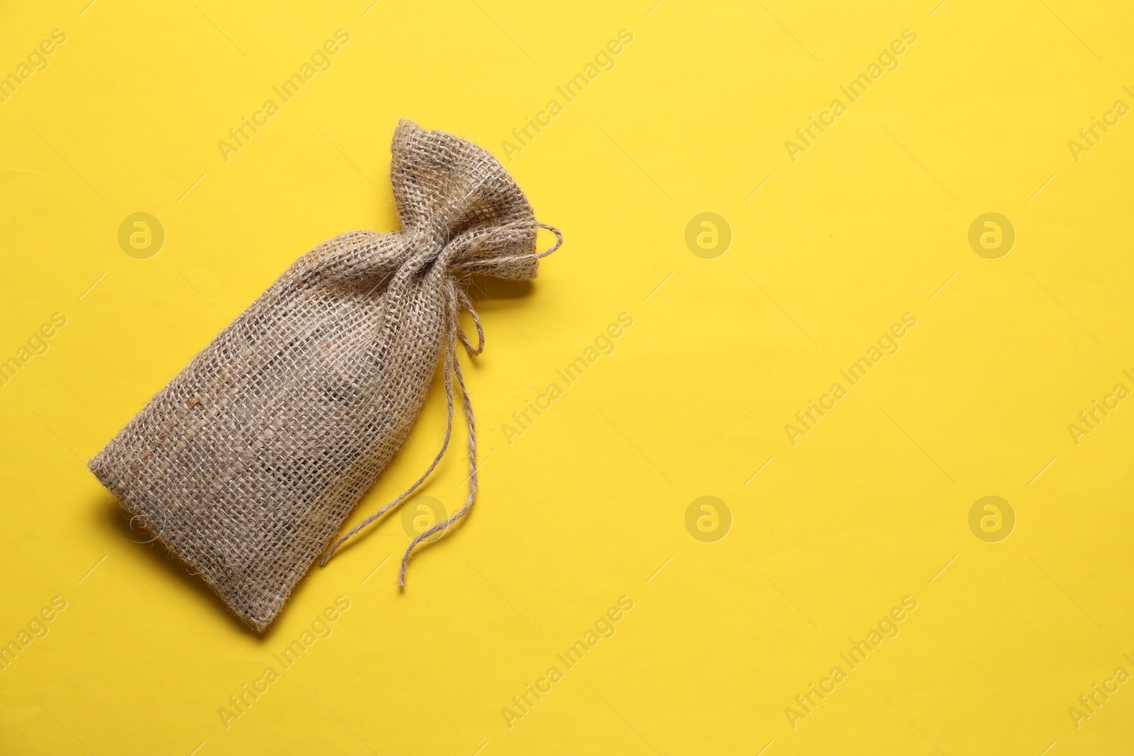 Photo of One burlap sack on yellow background, top view. Space for text