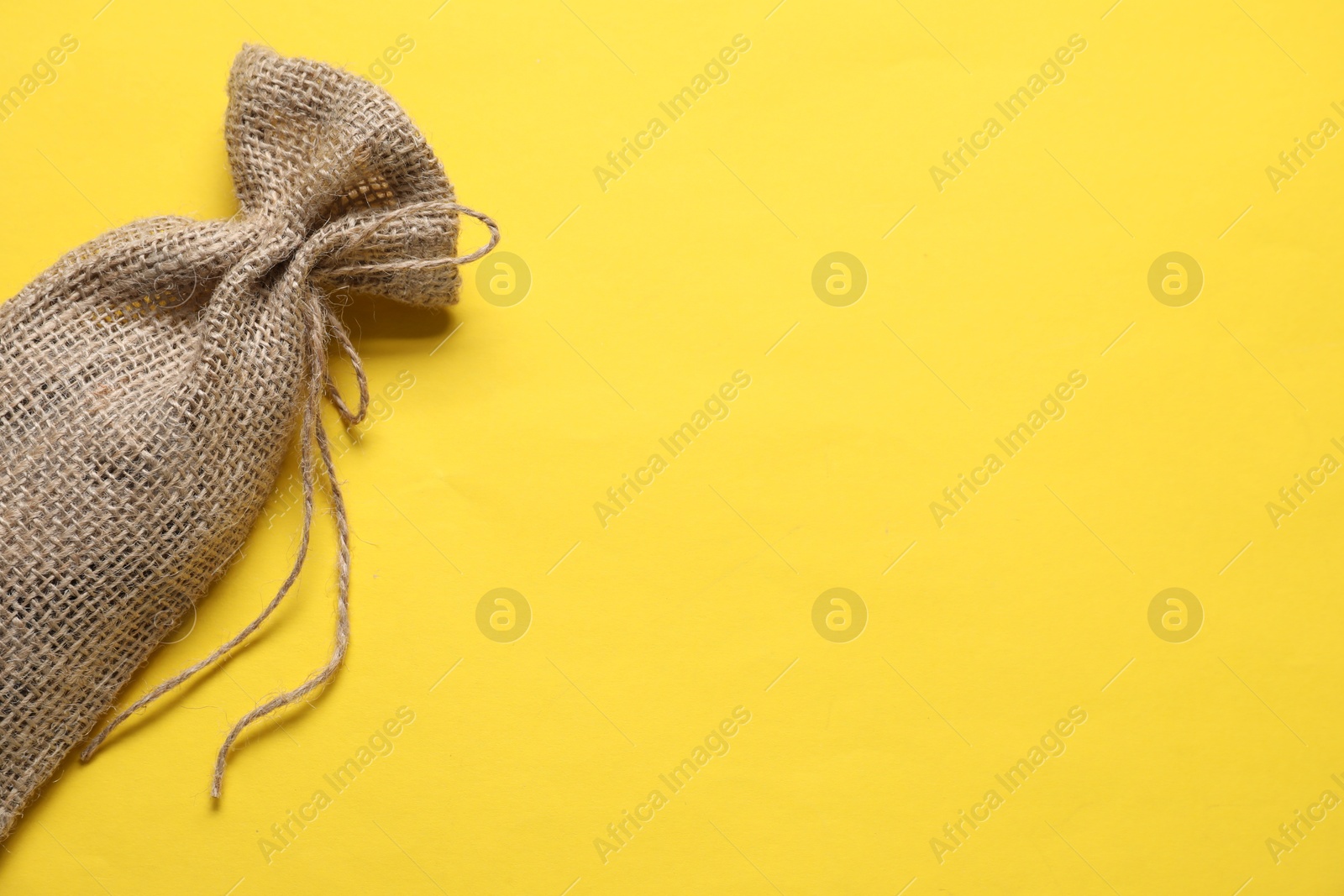 Photo of One burlap sack on yellow background, top view. Space for text