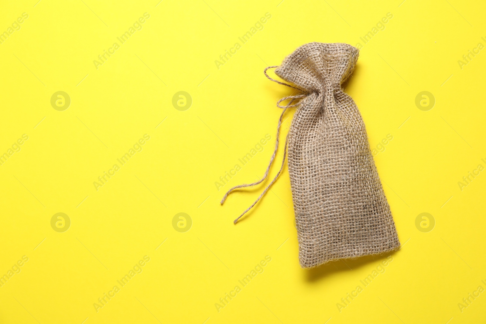 Photo of One burlap sack on yellow background, top view. Space for text