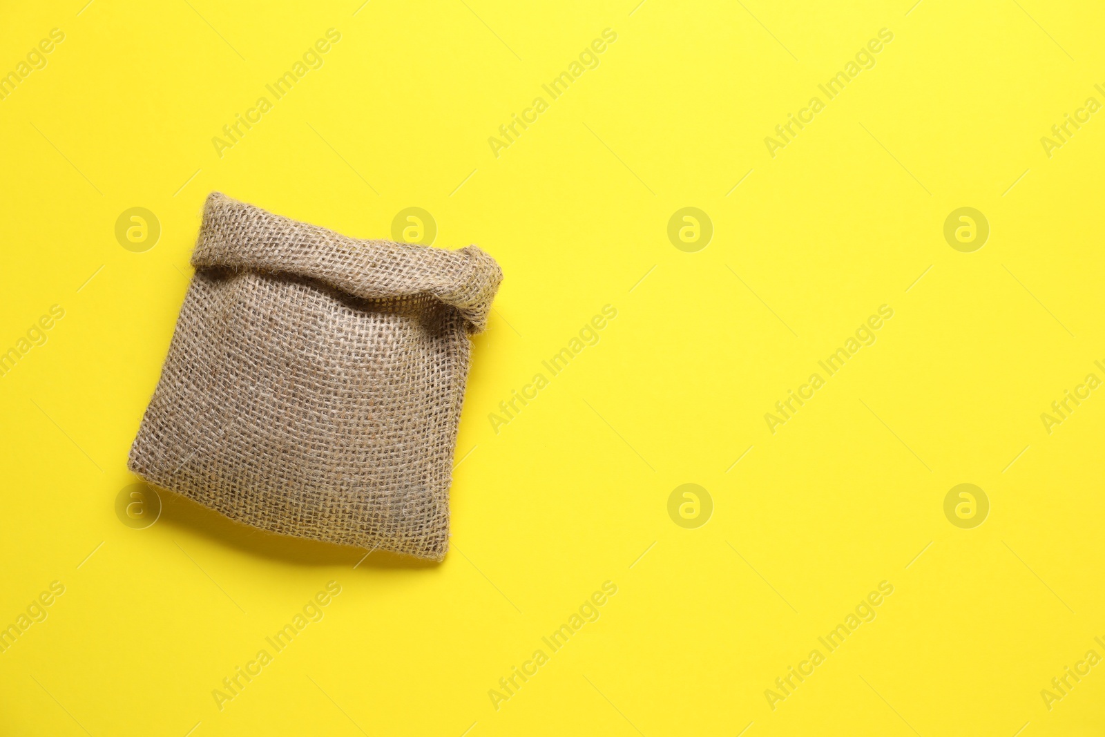 Photo of One burlap sack on yellow background, top view. Space for text