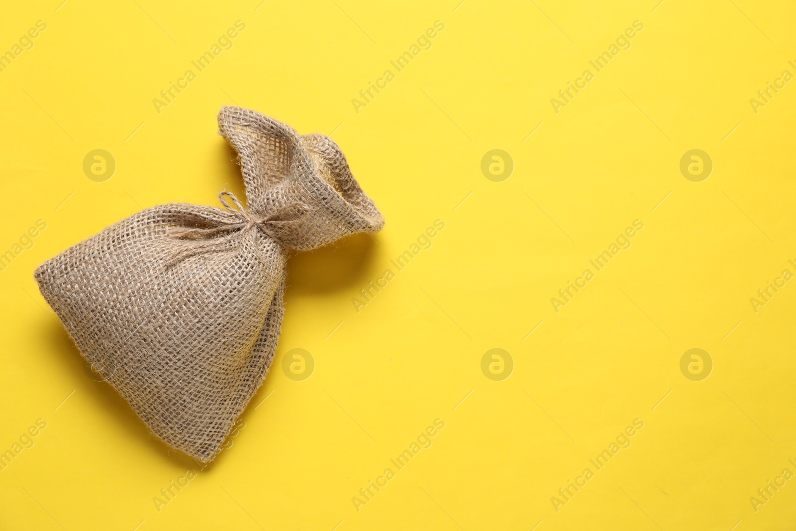 Photo of One burlap sack on yellow background, top view. Space for text