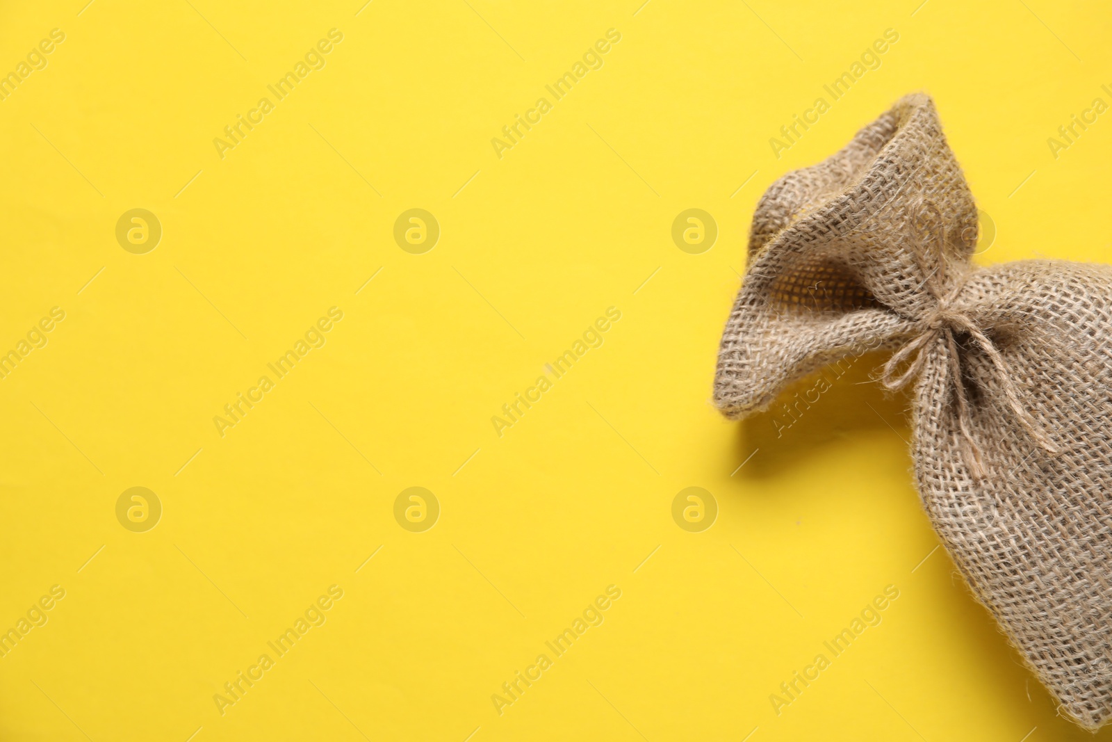 Photo of One burlap sack on yellow background, top view. Space for text