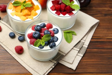 Photo of Tasty yogurt with fresh berries, fruits and mint in glasses on wooden table, closeup