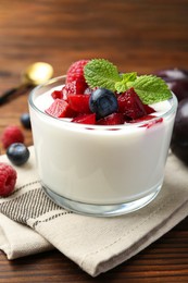 Tasty yogurt with fresh plums, berries and mint in glass on wooden table, closeup