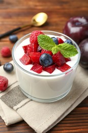 Photo of Tasty yogurt with fresh plums, berries and mint in glass on wooden table, closeup