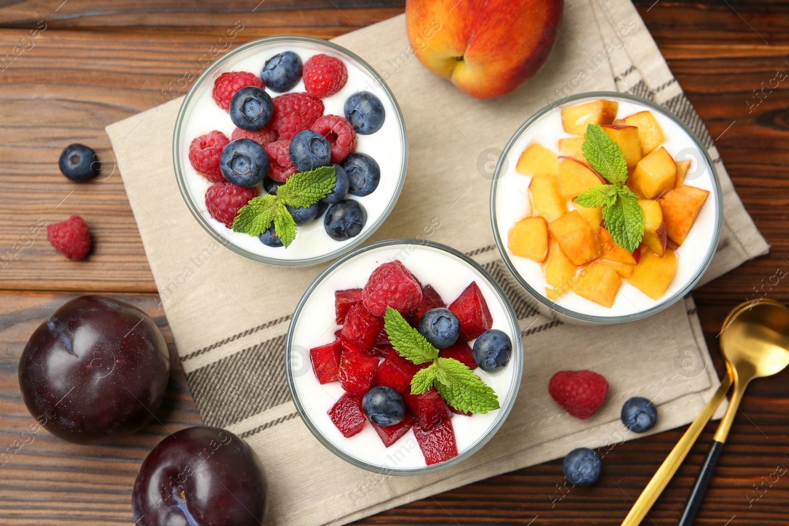 Photo of Tasty yogurt with fresh berries, fruits, mint in glasses and spoons on wooden table, flat lay