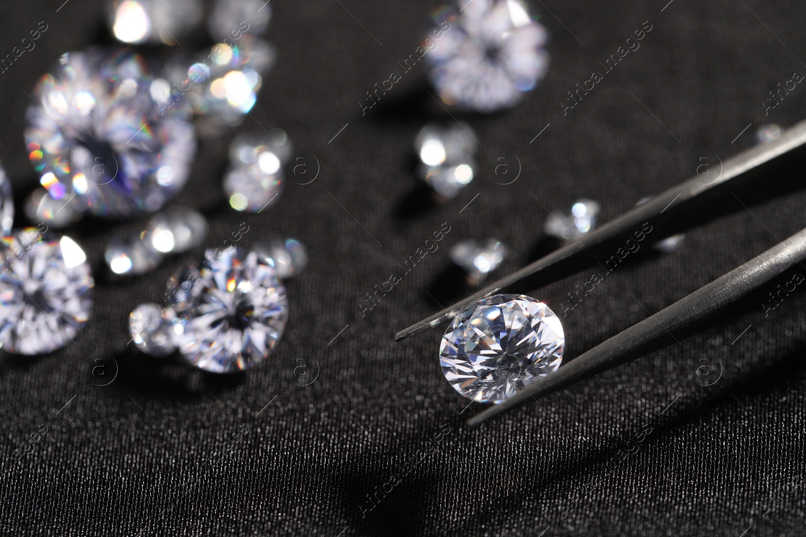 Photo of Tweezers with beautiful shiny diamonds on black fabric, closeup