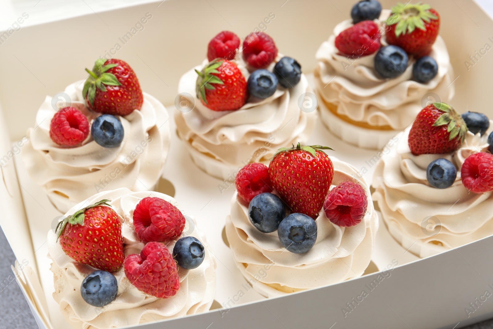 Photo of Tasty cupcakes with different berries in box on table, closeup